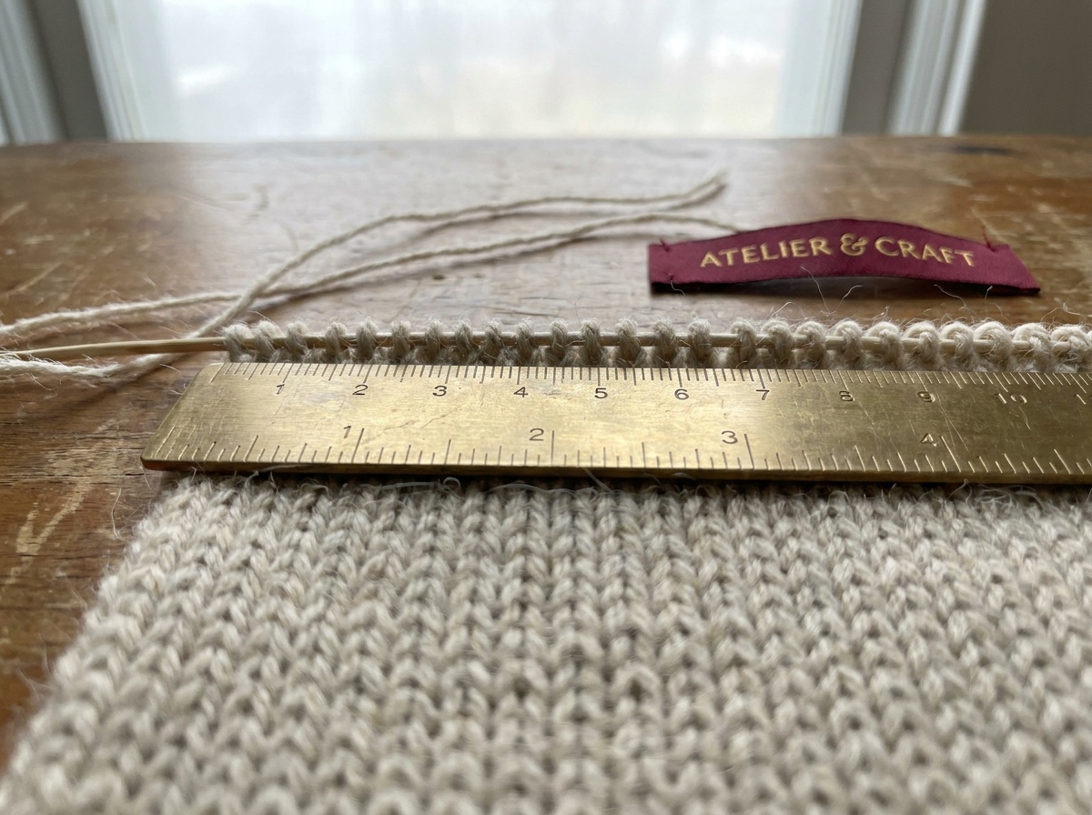 A ruler resting across the center of a flat knitted stockinette swatch, measuring a span of even stitches.